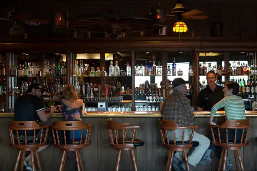saloon-style bar with 4 people sitting at the bar, bartender speaking with two of the customers from behind the bar